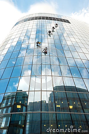 Five window washers work at a height on a high-rise building with a glazed facade against a blue sky with light clouds Editorial Stock Photo