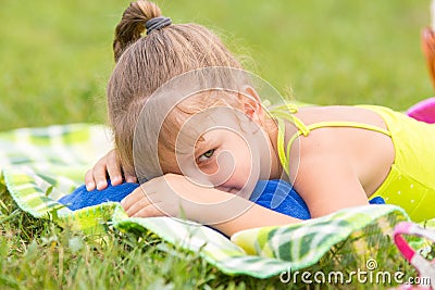Five-year girl lies on a bed on green meadow and artfully looks aside Stock Photo