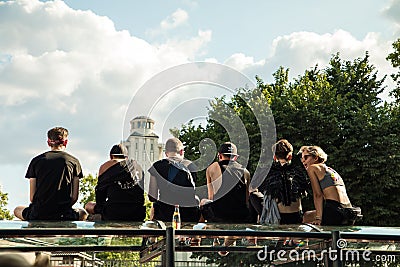 Five young guys dressed in black T-shirts and one girl with short hair are sitting on the glass roof of the bus stop and looking f Editorial Stock Photo