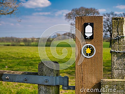 Fixed to a wooden post on a stile, a direction marker and white acorn logo of a Natural England National Trail Editorial Stock Photo