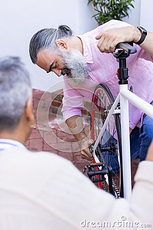 Fixing bicycle, senior man adjusting bike seat while woman watches attentively Stock Photo