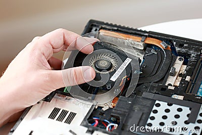 Fixing laptop. Repairman holds cooling fan and repairs from overheating. Disassembling computer, replacement, clean dust Stock Photo