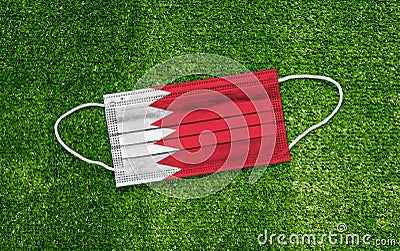 Flag Bahrain placed on a medical mask lies on the green grass. Covid-19 pandemic concept Stock Photo