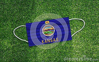 Flag Kansas placed on a medical mask lies on the green grass. Covid-19 pandemic concept Stock Photo