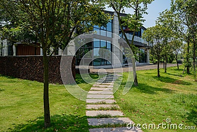 Flagstone path in lawn to two-storied modern building on sunny s Stock Photo