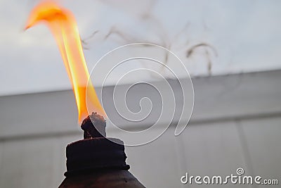 orange flame and burning wick on an oil torch against an overcast sky in the backyard Stock Photo