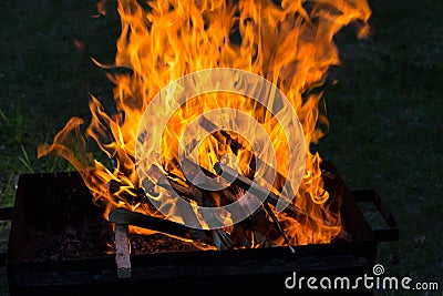 Flames from falling burning wood on the grill, against the background of grass Stock Photo