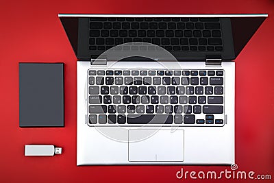 A flash drive, an external hard drive and an open laptop on a red desk Stock Photo