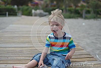 Flashy boy sits on a wooden walkway on the beach Stock Photo