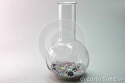 Flat-bottomed round flask with high narrow neck, of borosilicate glass filled with colorful pills Stock Photo