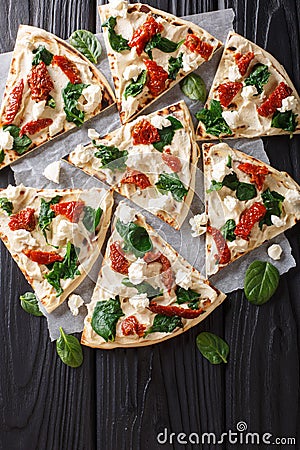 Flat bread with hummus, sun-dried tomatoes, spinach and goat cheese close-up. vertical top view Stock Photo