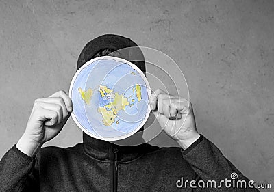 Flat Earther concept. Person who believes that Earth is flat disc. Anonymous hooded Man holding flat Earth model in front of face. Stock Photo