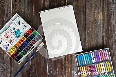 Flat lay art workplace, wooden table with paint brushes, watercolor paints, paper canvas and crayon pastel chalks Stock Photo