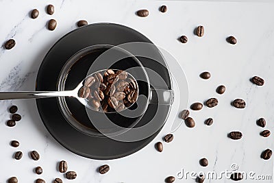 Flat lay beverage background of roasted coffee beans in spoon over a cup of coffee on white marble background with roasted coffee Stock Photo