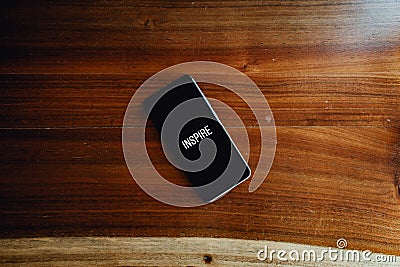 Flat lay of a black phone over a wood background with the word inspire written in it Stock Photo