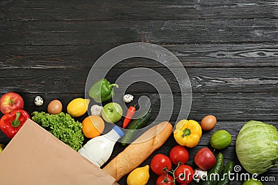 Flat lay composition with overturned paper bag and groceries on black wooden background Stock Photo