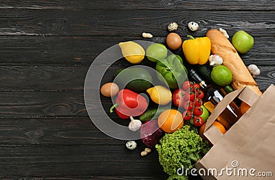 Flat lay composition with overturned paper bag and groceries on black wooden . Space for Stock Photo