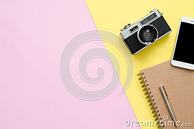 Top view of brown notebook, pencil, tablet and camera on pink and yellow pastel color screen with a copy space. Stock Photo