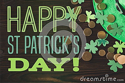 Flat lay with green hat, coins and shamrocks on wooden surface with happy st patricks day Stock Photo