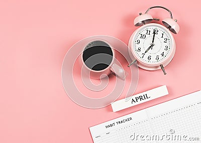 Flat lay of habit tracker book, wooden calendar April, pink vintage alarm clock 7 o`clock and pink cup of black coffee on blue Stock Photo