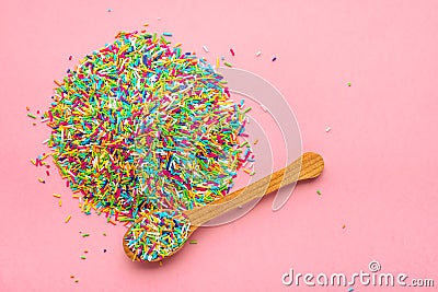 Flat lay of heap colorful sprinkles on wooden spoon over pink background, top view Stock Photo