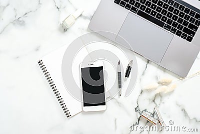 Flat lay home office desk. Female workspace with laptop computer, dry flowers, paper notepad, smartphone on marble background. Top Editorial Stock Photo