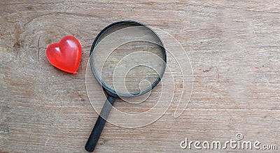 magnifying glass and decorative red hearts isolated on a brown wooden background minimalist trend.valentines day concept Stock Photo