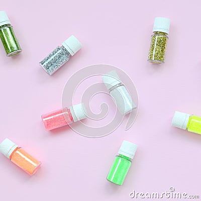 A flat lay pattern with colorful glitter bottles lies on pastel pink background Stock Photo