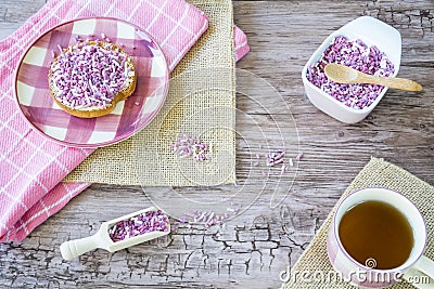 Flat lay with rusk, sweet pink purple sprinkles and cup of tea. Against wooden background Stock Photo