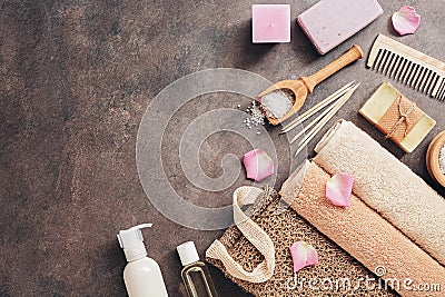 Flat lay a set of various bath and spa accessories. Terry towel, soap, comb, oil, shampoo, loofah washcloth, sea salt on a dark Stock Photo