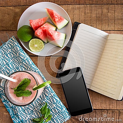 A flat lay square ratio breakfast tabletop photo with watermelon smoothie phone, book and sliced fruit on plate Stock Photo