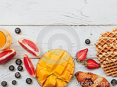 Flat lay summer breakfast with waffle and fruits. Frame mockup with mango, strawberry, and cherry on wooden background Stock Photo