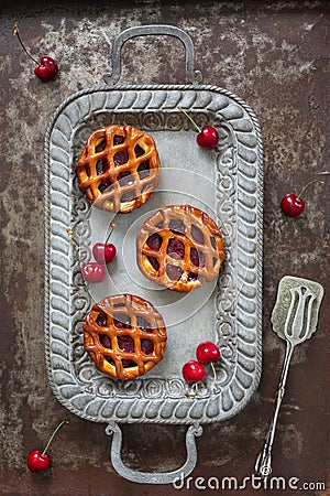 Flat lay of three individual cherry pies and fresh cherries on a serving tray on rustic background Stock Photo