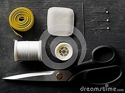 Flat lay top view sewing tools with measurement tape, chalk, thread, needles and scissors on black dark wood table Stock Photo