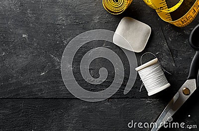 Flat lay top view sewing tools with measurement tape, chalk, thread and scissors on black dark wood table Stock Photo