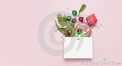 Flat lay top view White gift bag holographic glitter confetti red green christmas balls pine branches gift boxes on pink Stock Photo