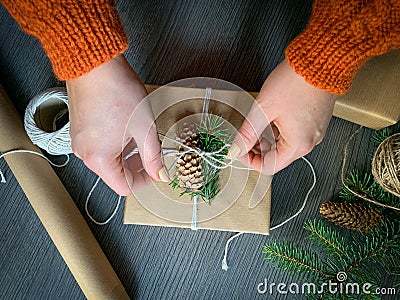 Flat lay of hands crafted gift box on wooden table with roll of craft paper, twine rolls, fir branches and pine cones Stock Photo