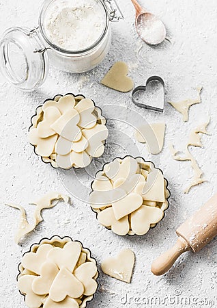 Flat lay Valentine`s day baking background. Raw apple tartlets in the baking dish and baking ingredients on light background Stock Photo