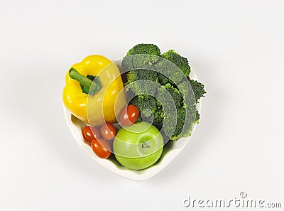 Flat lay of vegetables capsicum, broccoli tomatoes and green apple in heart shape plate on white background with copy space, Stock Photo