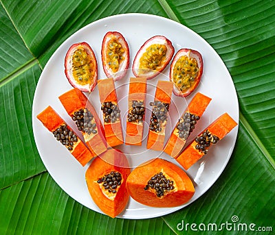 Flat lay. Vegetarian nutrition. papaya pieces and passion fruit on white plate with green banana leaves background, top view Stock Photo