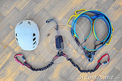 Flat lay of via ferrata gear white helmet, two lanyards with shock absorber system, climbing harness on wooden background. Stock Photo