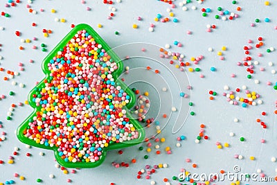 Flat lay view of Christmas tree shaped cookie cutter filled with rainbow sugar sprinkles. Stock Photo