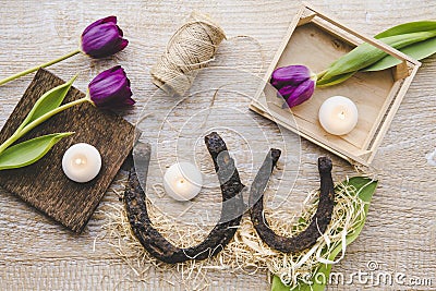 Flat lay view of two rusty small and big horseshoes on light wooden board background, decorated with white small candles. Stock Photo