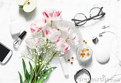 Flat lay women`s accessories set - tulips bouquet, cosmetics, glasses, phone, apple, headphones on light background top view. Bea Stock Photo