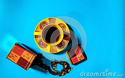 Flat view of tea time concept with colorful tea cup and tea container, loose black tea on blue background with space for text. Stock Photo