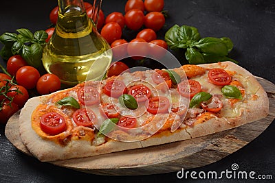 Flatbread pizza garnished with fresh cherry tomatoes, basil, cheese and olive oil on wooden pizza board. Stock Photo