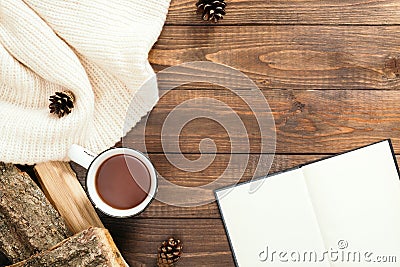 Flatlay composition with white knitted scarf, cup of tea, book with empty pages, firewood on wooden desk table. Hygge style, cozy Stock Photo