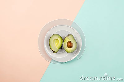 Flatlay with cut avocado on white plate on pastel background Stock Photo