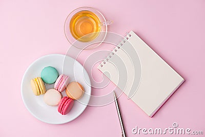 Flatlay of notebook, cake macaron and cup of tea on pink table. Stock Photo