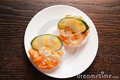 Flatlay, sandwich with red fish and cucumber on a white plate. Salted salmon on crispy rice bread on a wooden background Stock Photo